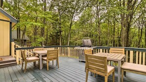 Una terraza de madera con mobiliario exterior, una parrilla y vistas a una zona boscosa.
