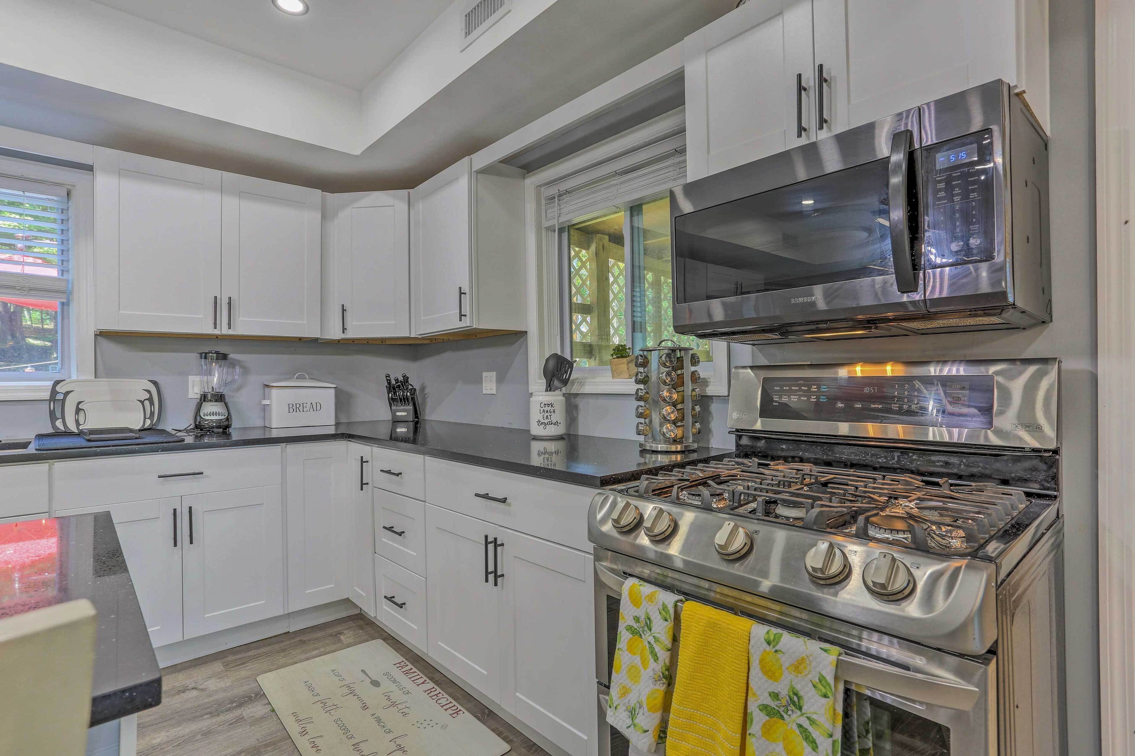 A modern kitchen with white cabinets, a stainless steel stove, a microwave, and a window with blinds.