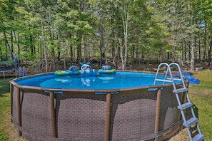 Une piscine hors sol entourée d’une clôture en osier, avec une échelle d’un côté et des jouets gonflables dans l’eau.