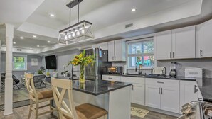 A modern kitchen with white cabinets, a central island with seating, and a large window providing natural light. - Stunning South Fallsburg Home w/ Pool & Deck! (South Fallsburg)