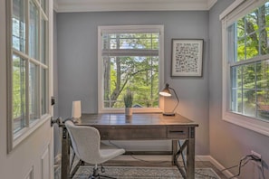 Une pièce comprenant un bureau, une chaise et une fenêtre donnant sur des arbres.