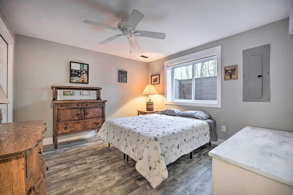 Un dormitorio con cama, cómoda de madera, ventilador de techo, ventana y luz empotrada.