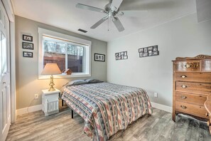 Un dormitorio con cama, cómoda, ventana con vistas, ventilador de techo y cuadros colgados en la pared.