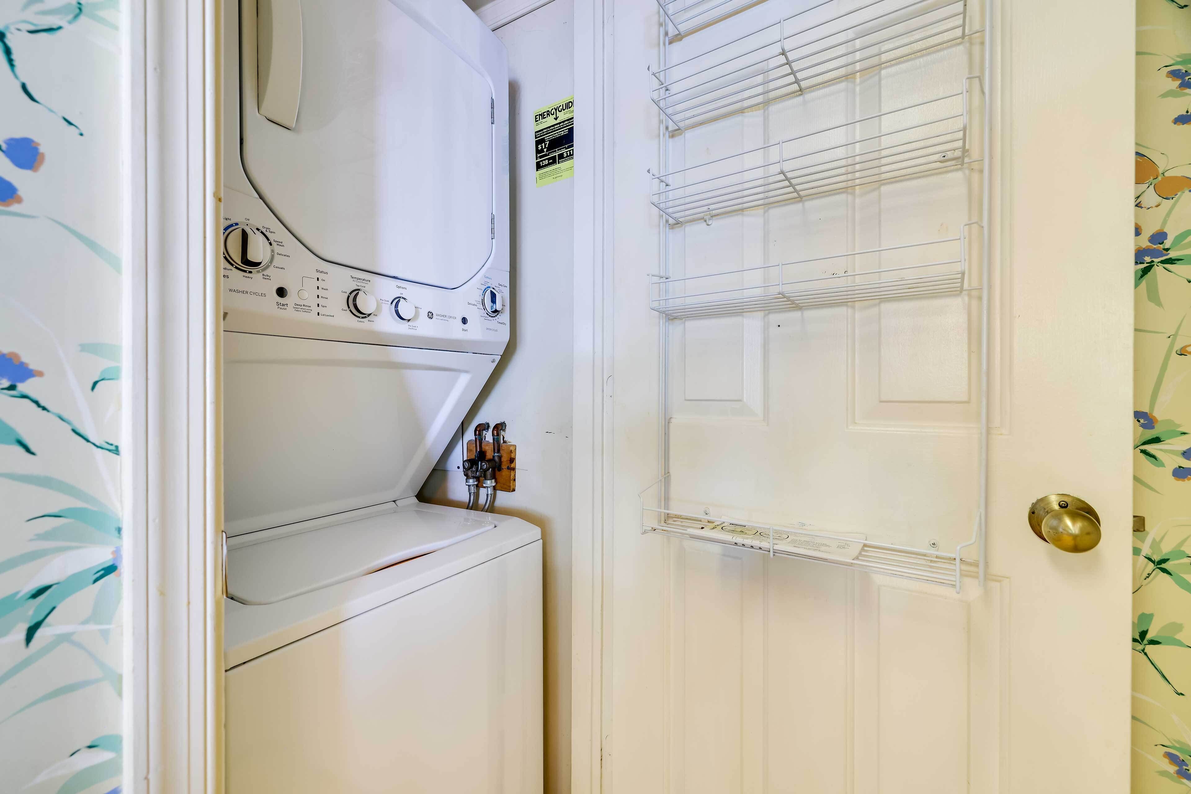 A laundry room with a front-loading washer and dryer, a door with a brass handle, and a shelf with a power strip.