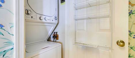 A laundry room with a front-loading washer and dryer, a door with a brass handle, and a shelf with a power strip.