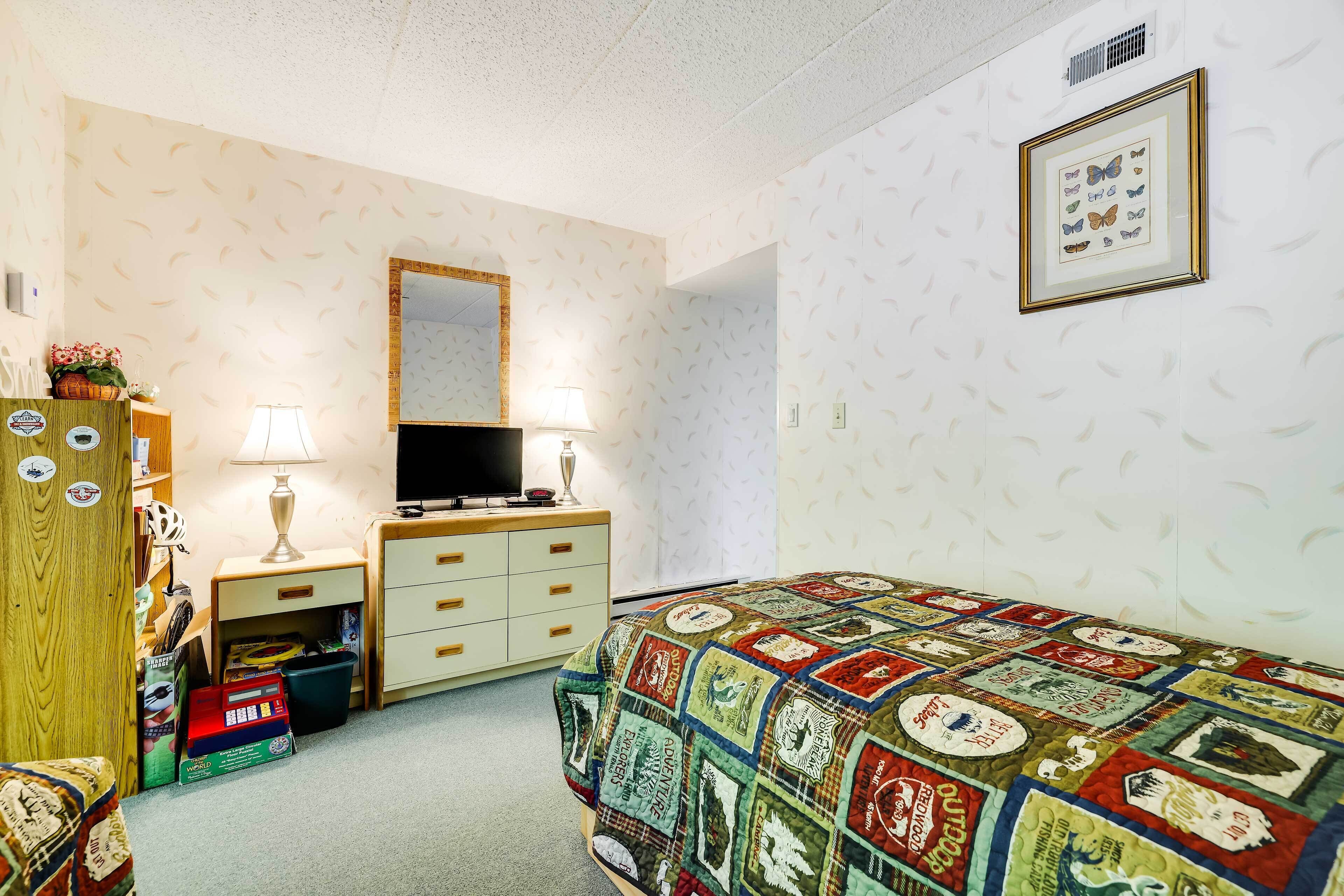 A bedroom with a quilted bedspread, a dresser, a mirror, and a framed picture on the wall.