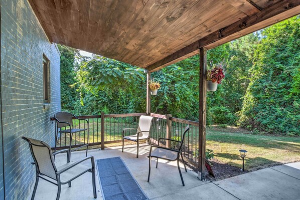 A covered patio with two chairs and a table, a wooden ceiling, and a brick wall.