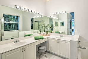 A modern bathroom with two sinks, a large mirror with lights, and a window with a view of trees. - Gorgeous Miramar Villa w/ Lake & Pool Views (Miramar)