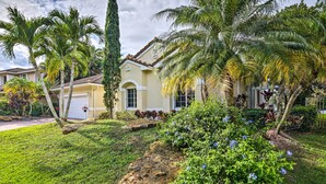 Una casa residencial con césped cuidado, palmeras y diversas plantas con flores.