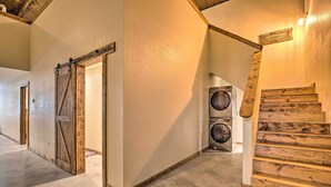 Een gang met een houten deur, een wasmachine en een houten trap.