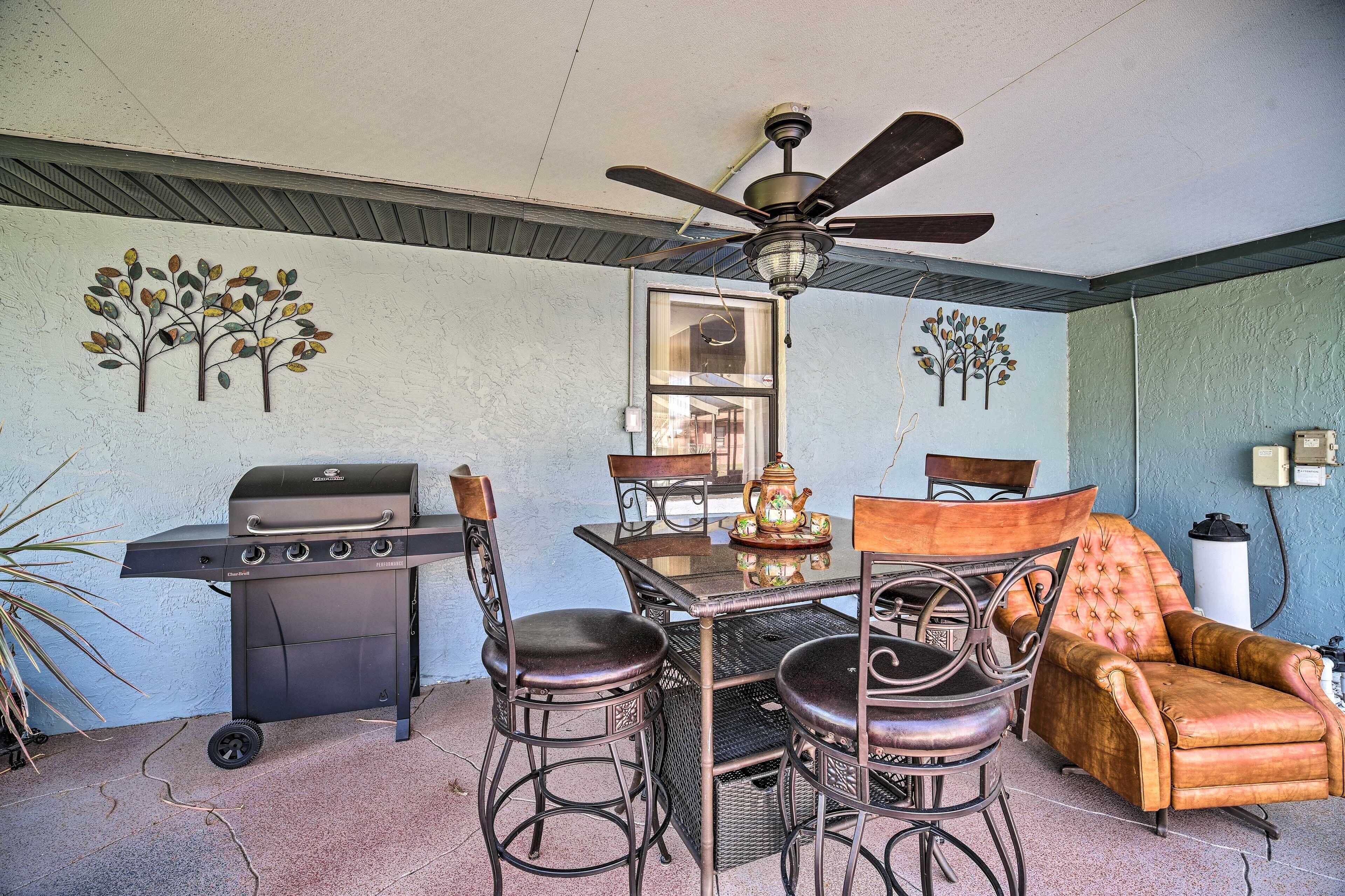 A patio with a grill, dining table, chairs, and a ceiling fan.