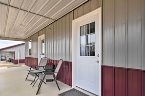 A covered porch with metal siding, a white door, and two folding chairs.