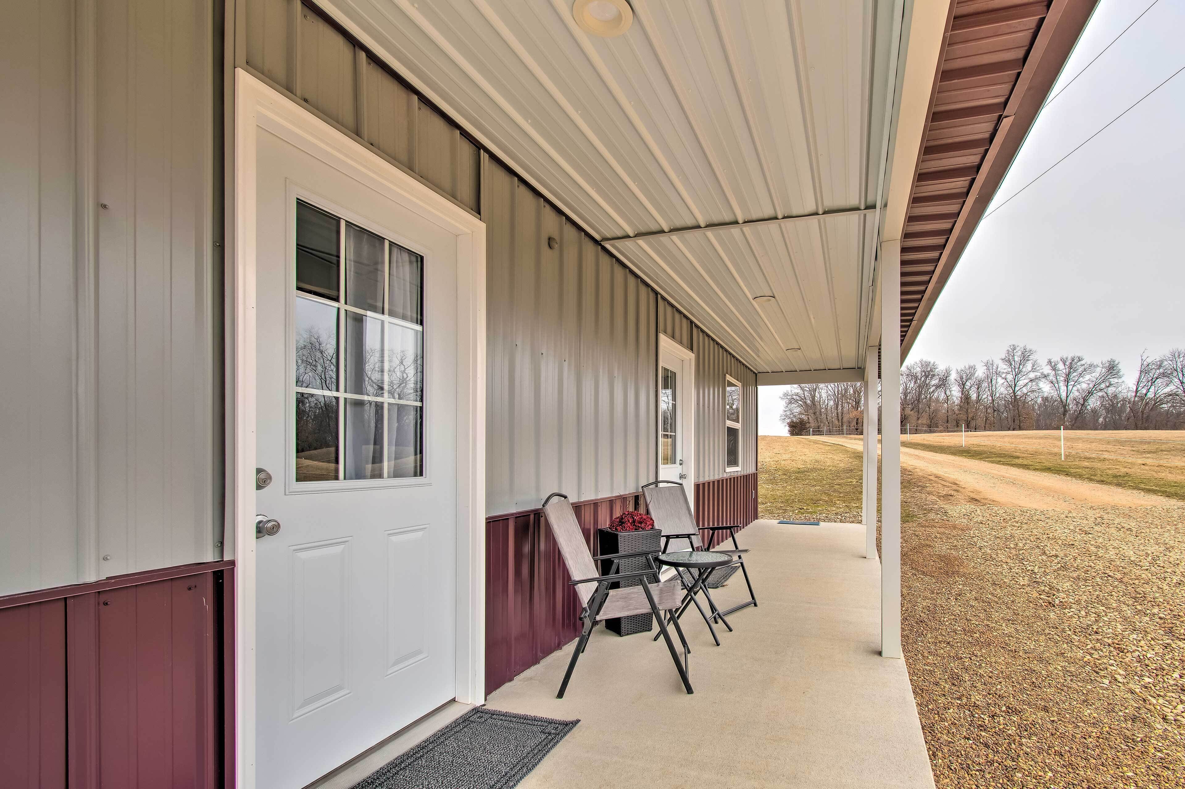 A covered porch with a white door, two folding chairs, and a concrete walkway.
