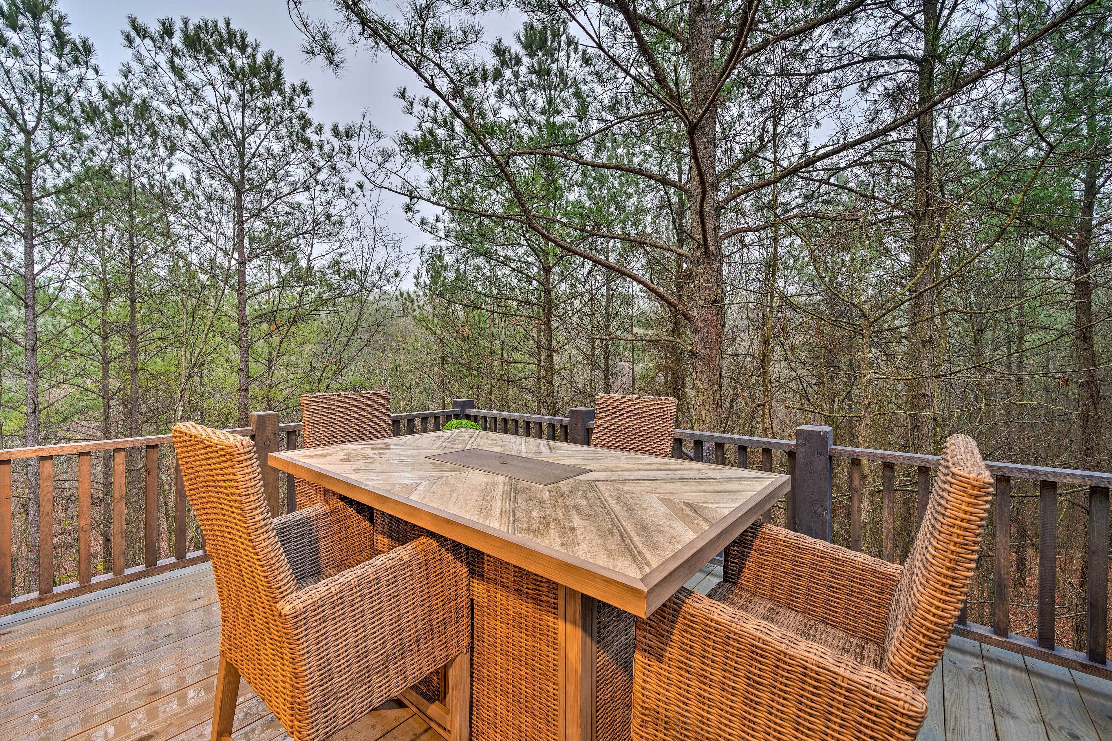 A wooden deck with a table and wicker chairs, surrounded by trees.