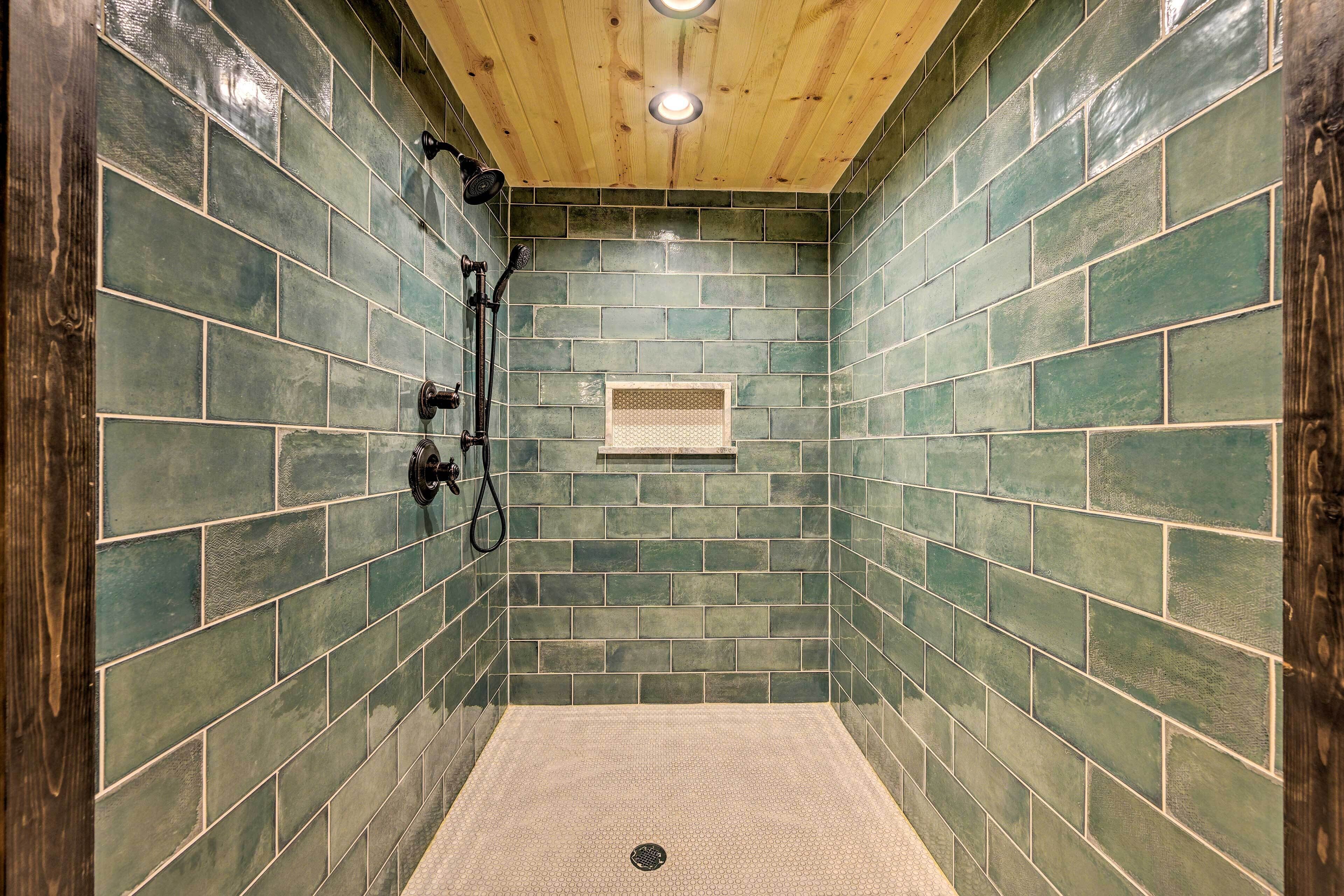 A shower area with green tiles, wooden ceiling, and a small window.