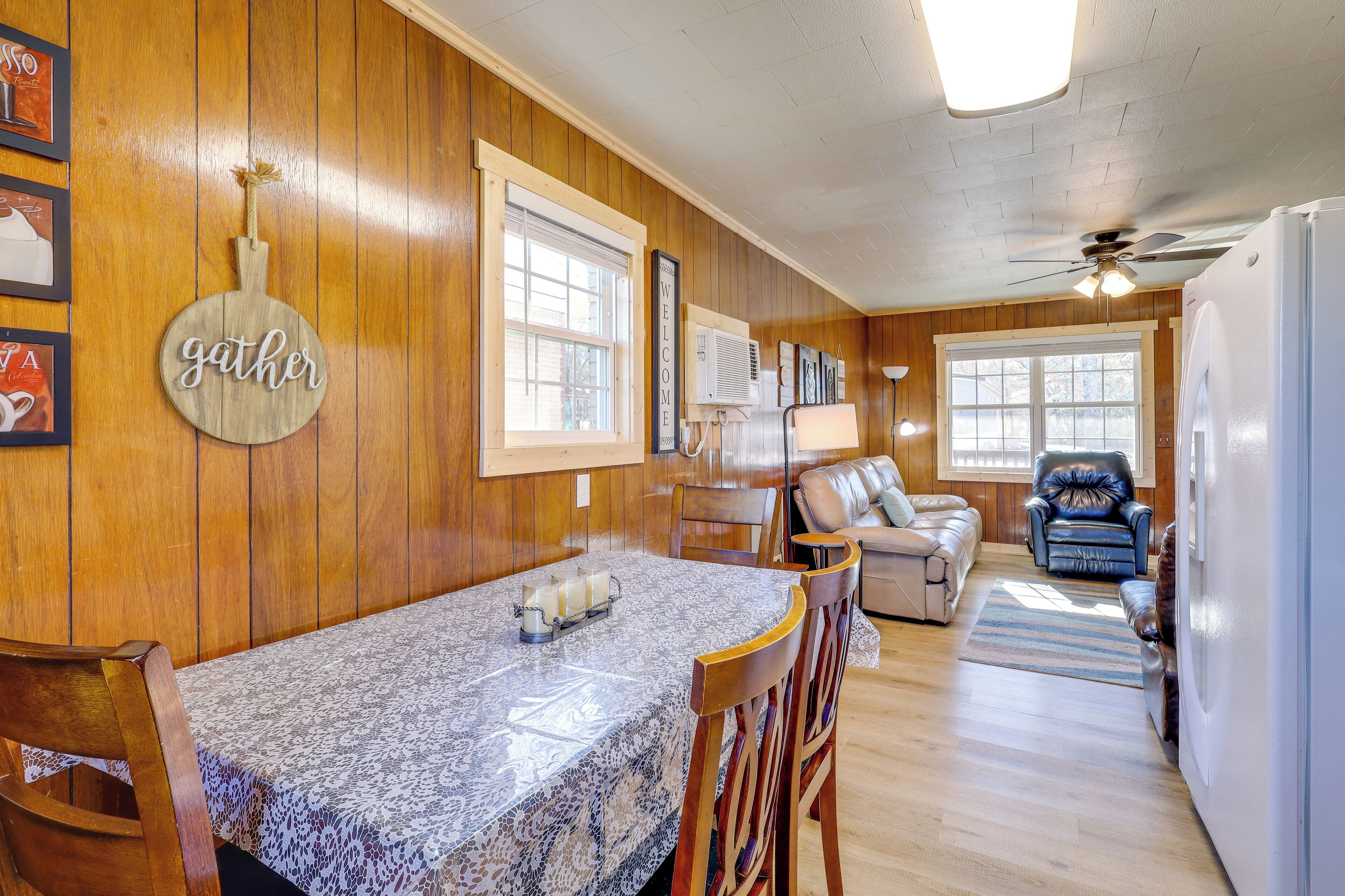A wooden-paneled room with a dining table, chairs, a sofa, a recliner, and a ceiling fan.
