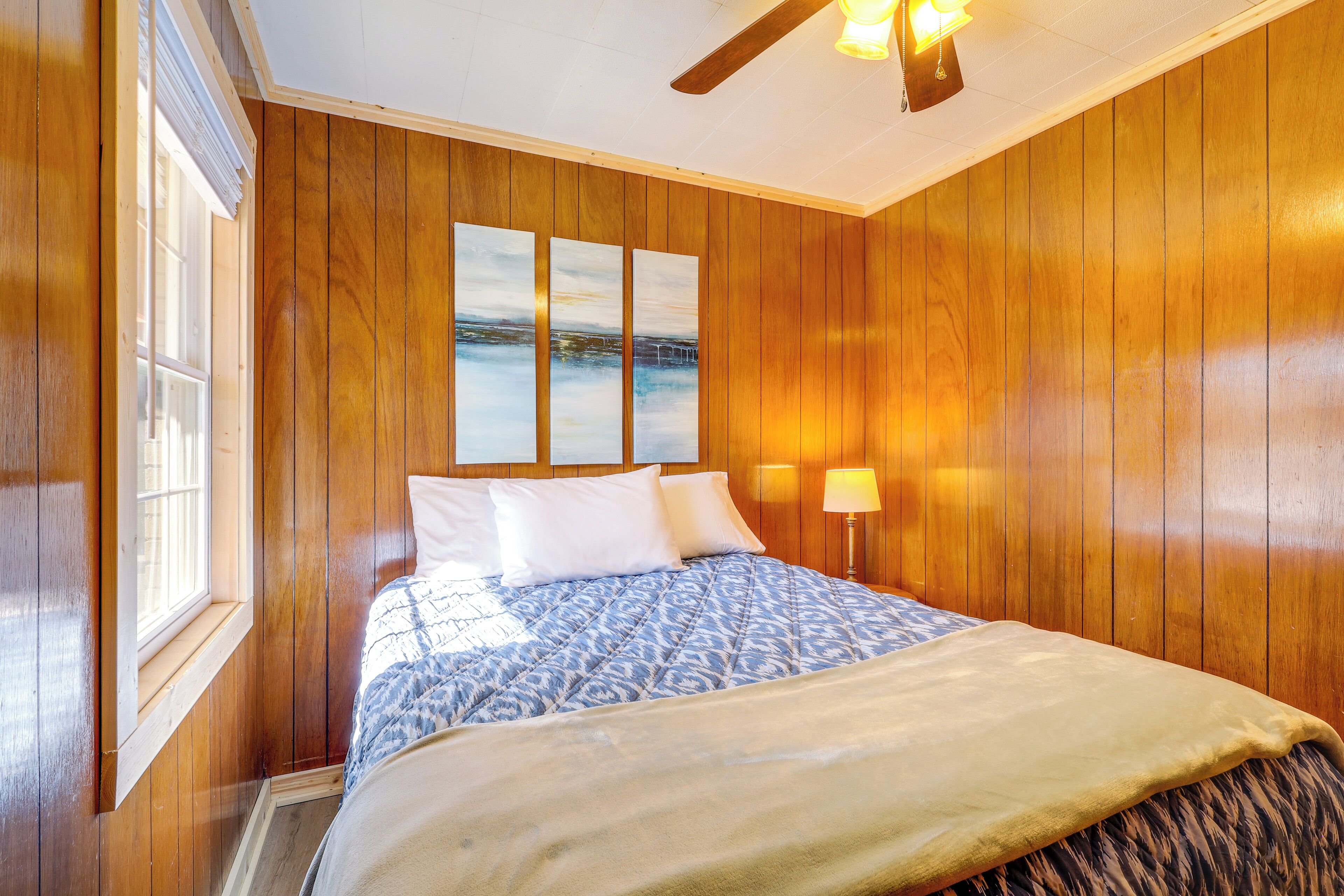 Une chambre d’hôtel avec des lambris en bois, un lit recouvert d’une couvre-lit à motifs, une table de chevet avec une lampe et un ventilateur de plafond.