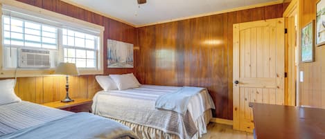 Ein Zimmer mit zwei Betten, Holzwänden, einem Deckenventilator und einem großen Fenster.
