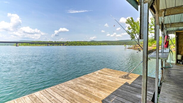A wooden dock extending into a calm lake with a bridge in the background. - Pet-friendly Cabin With Designated Boat Slip! (Higden)