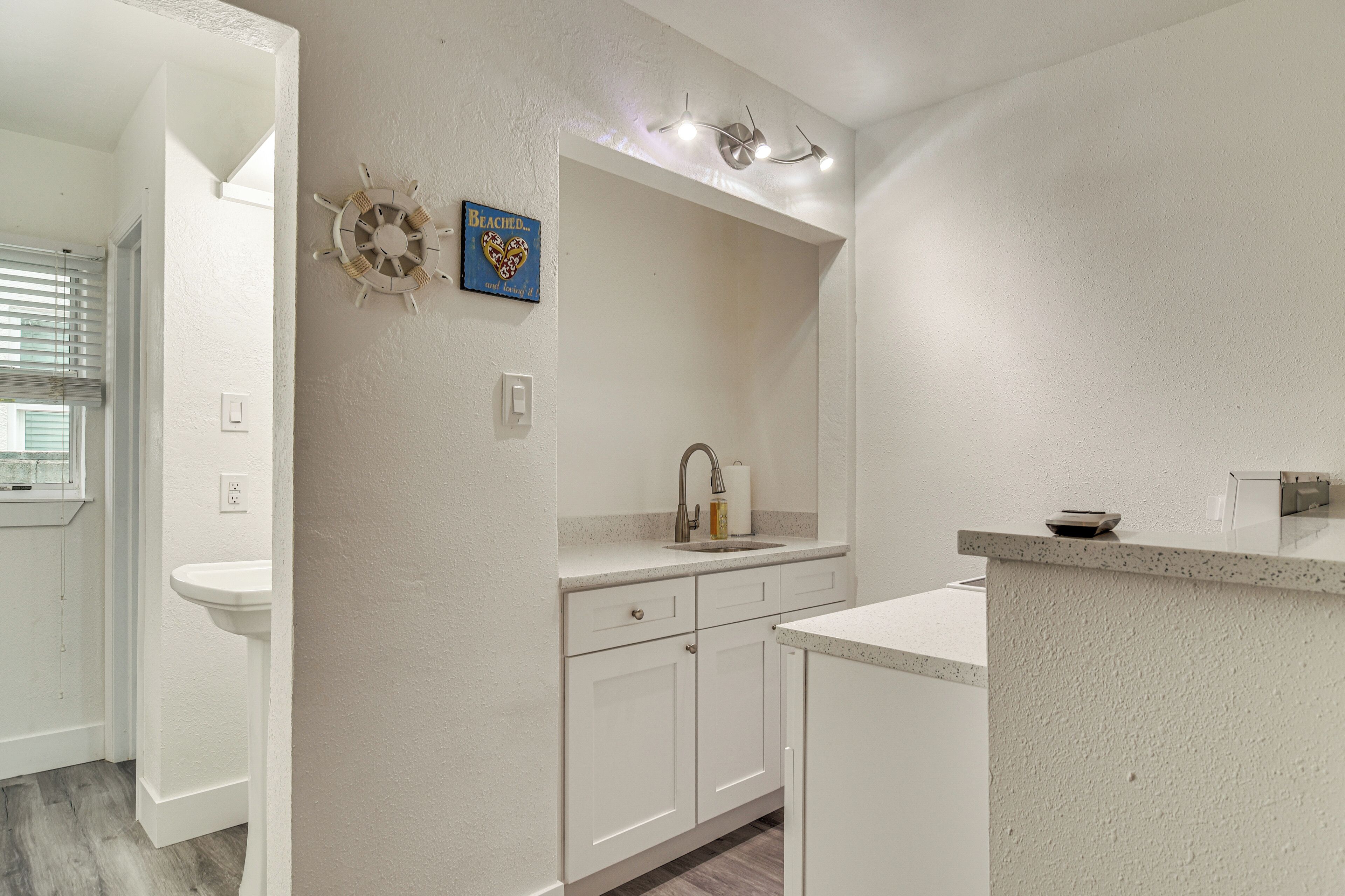 A modern bathroom with a white sink, vanity, and a mirror. There is a decorative wall piece above the sink and a small shelf with a bowl.