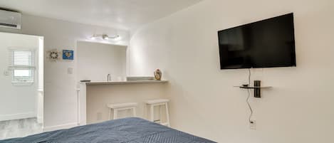 A bedroom with a bed, a TV mounted on the wall, a small window, and a bathroom with a sink and mirror.