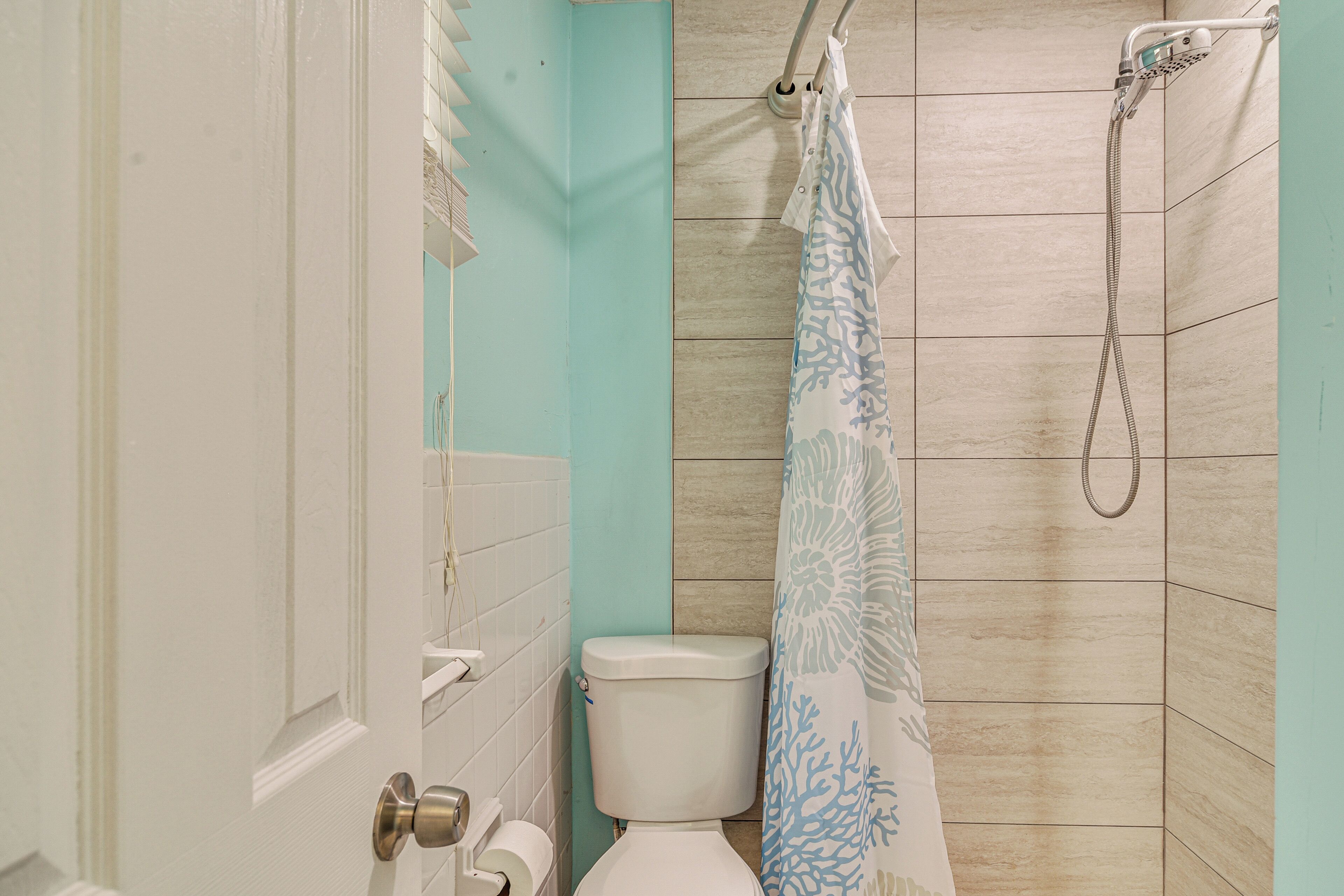 A bathroom with a toilet, a shower with a blue shower curtain, and a white door.