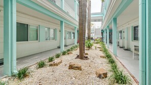 A hotel corridor with a central palm tree, white walls, and a tiled floor. - Tropical Pass-a-grille Gem w/ Direct Beach Access! (St. Pete Beach)