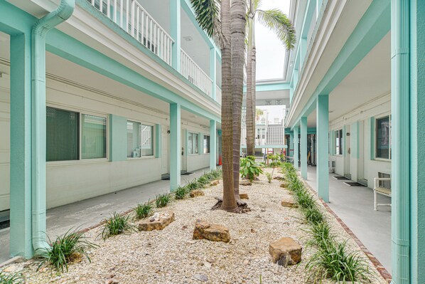 A hotel corridor with a central palm tree, white walls, and a tiled floor.