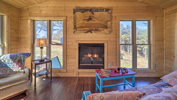 A cozy cabin interior with a fireplace, wooden walls, and large windows. - Nature Escape in Wytheville w/ Covered Porch! (Speedwell)