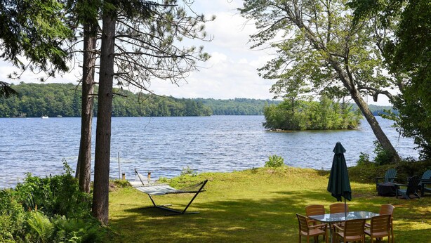 A lakeside patio with a hammock, a table with chairs, and an umbrella. - Life on the Lake With Private Dock & Fire Pit! (Winthrop)