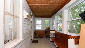 A narrow hallway with white siding, wooden benches, and large windows offering views of trees. - Life on the Lake With Private Dock & Fire Pit! (Winthrop)