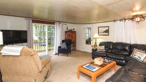 A living room with a beige sofa, a black leather couch, a wooden coffee table, a television, and a bookshelf. - Life on the Lake With Private Dock & Fire Pit! (Winthrop)