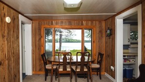 A dining area with a table and chairs, a view of a lake, and wooden walls. - Life on the Lake With Private Dock & Fire Pit! (Winthrop)