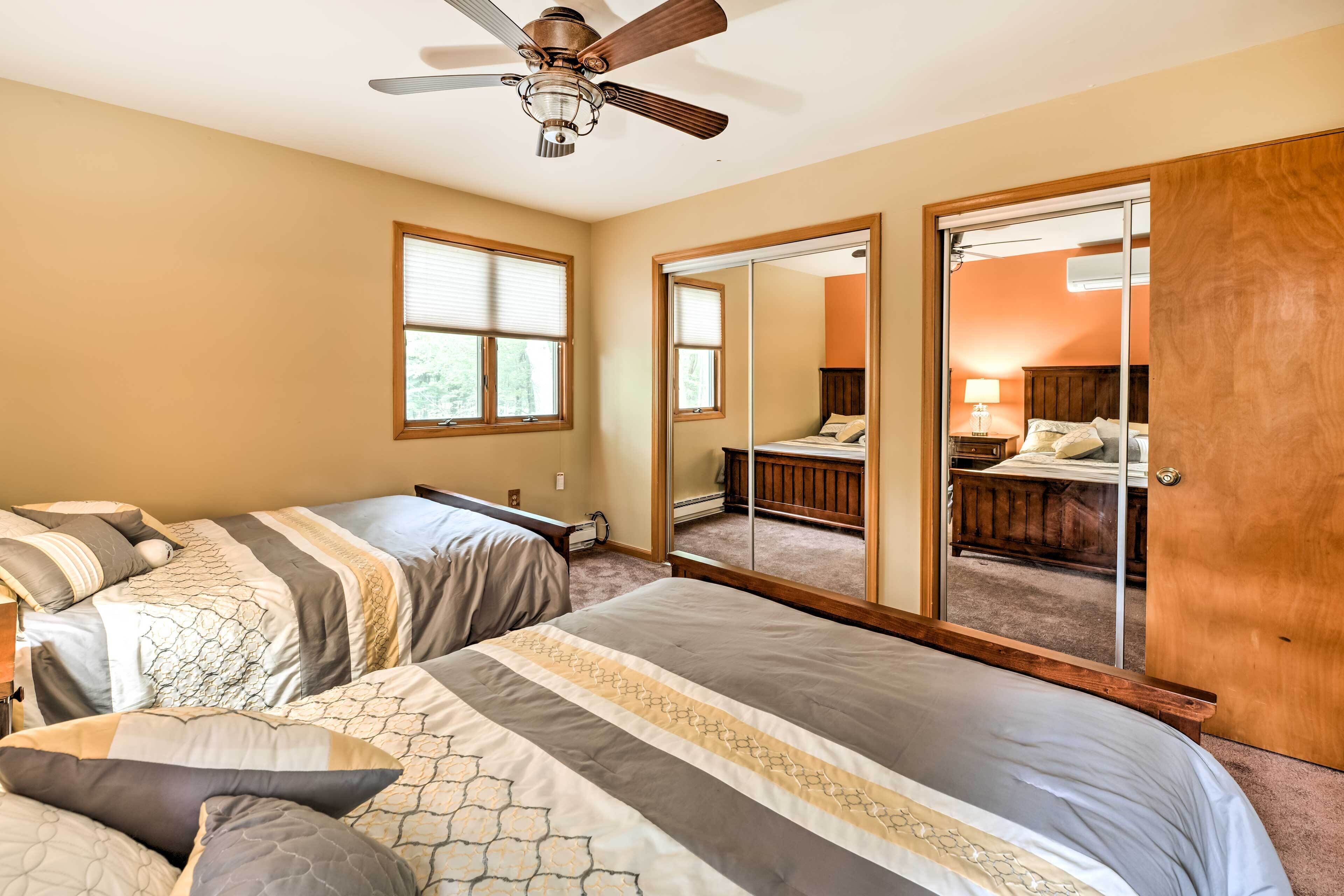 A bedroom with two beds, a ceiling fan, and a large mirror.