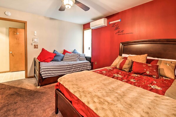 Un dormitorio con dos camas, una pared roja y un ventilador de techo.