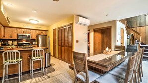 A modern kitchen with wooden cabinets, a stainless steel refrigerator, and a dining area with a glass table and wooden chairs.