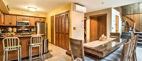 Una cocina moderna con armarios de madera, un refrigerador de acero inoxidable y un comedor con una mesa de vidrio y sillas de madera.