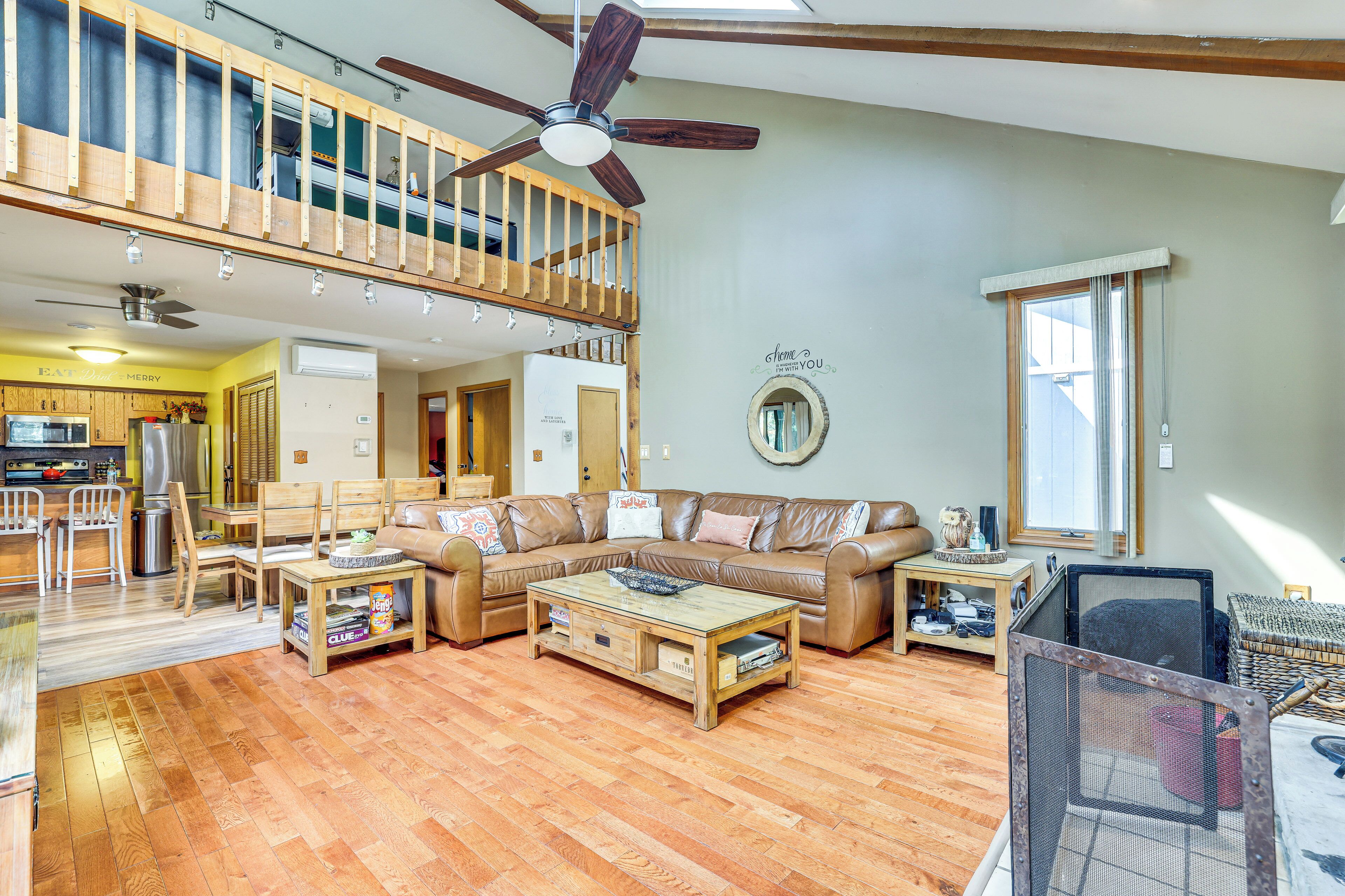 A spacious living area with a high ceiling, a ceiling fan, a dining area with wooden furniture, and a kitchen in the background.