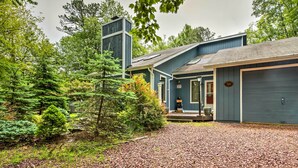 A house with a gravel driveway, a garage, and a large coniferous tree in the front yard.