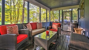 A covered porch with wicker furniture, red cushions, and a glass table.