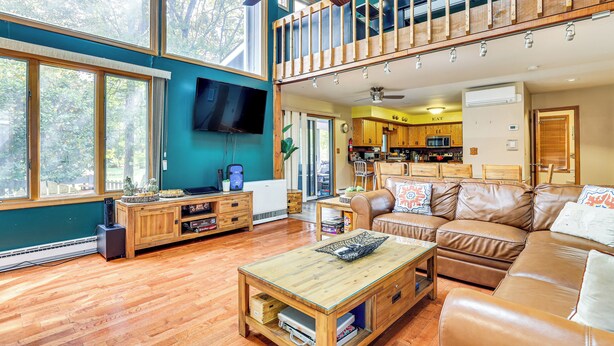 A spacious living area with a wooden coffee table, leather sofa, and a TV mounted on the wall.
