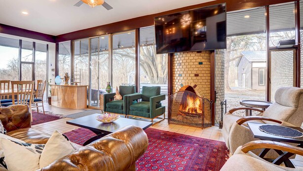 A spacious living room with a fireplace, comfortable seating, a TV mounted on the wall, and large windows offering a view of the outdoors. - Stylish + Serene West Friendship Hidden Gem! (West Friendship)