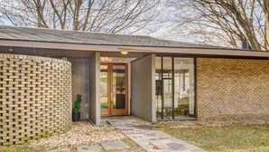 A modern building with a brick facade, a stone pathway leading to a glass door entrance, and a small garden area with a hedge. - Stylish + Serene West Friendship Hidden Gem! (West Friendship)