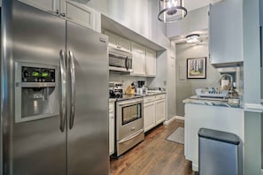 A modern kitchen with stainless steel appliances, white cabinetry, and a wooden floor.