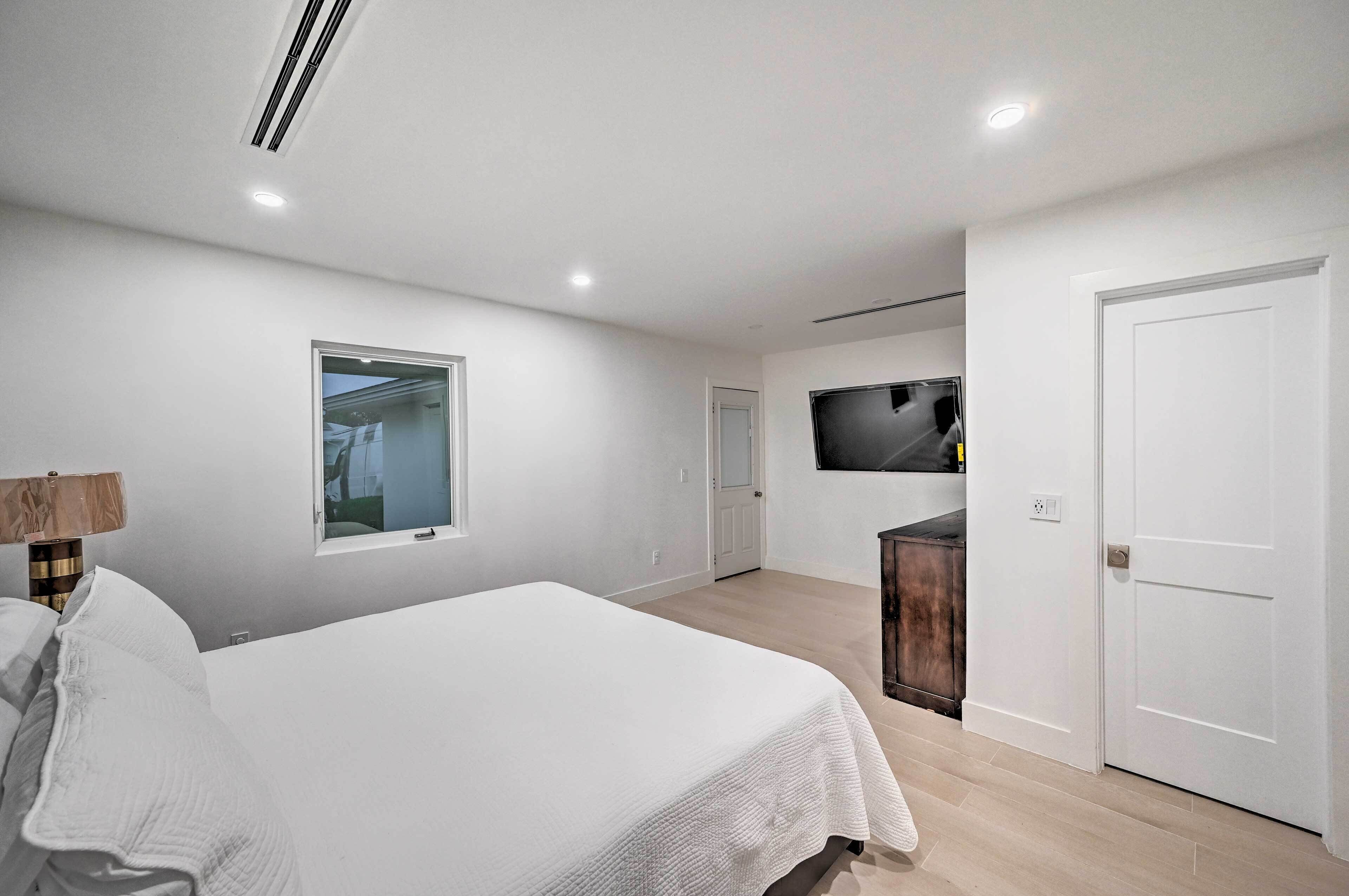 A bedroom with a bed, a TV mounted on the wall, and a door leading to another room.