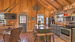 A rustic cabin interior with a wooden interior, a dining area with benches, a kitchen with modern appliances, and a television mounted on the wall. - Scenic Greers Ferry Cabin w/ Deck + Fire Pit! (Higden)