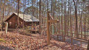A rustic cabin with a metal roof and wooden deck, surrounded by a forest. - Scenic Greers Ferry Cabin w/ Deck + Fire Pit! (Higden)