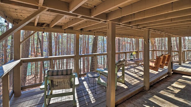A covered wooden deck with seating and a table, surrounded by trees. - Scenic Greers Ferry Cabin w/ Deck + Fire Pit! (Higden)