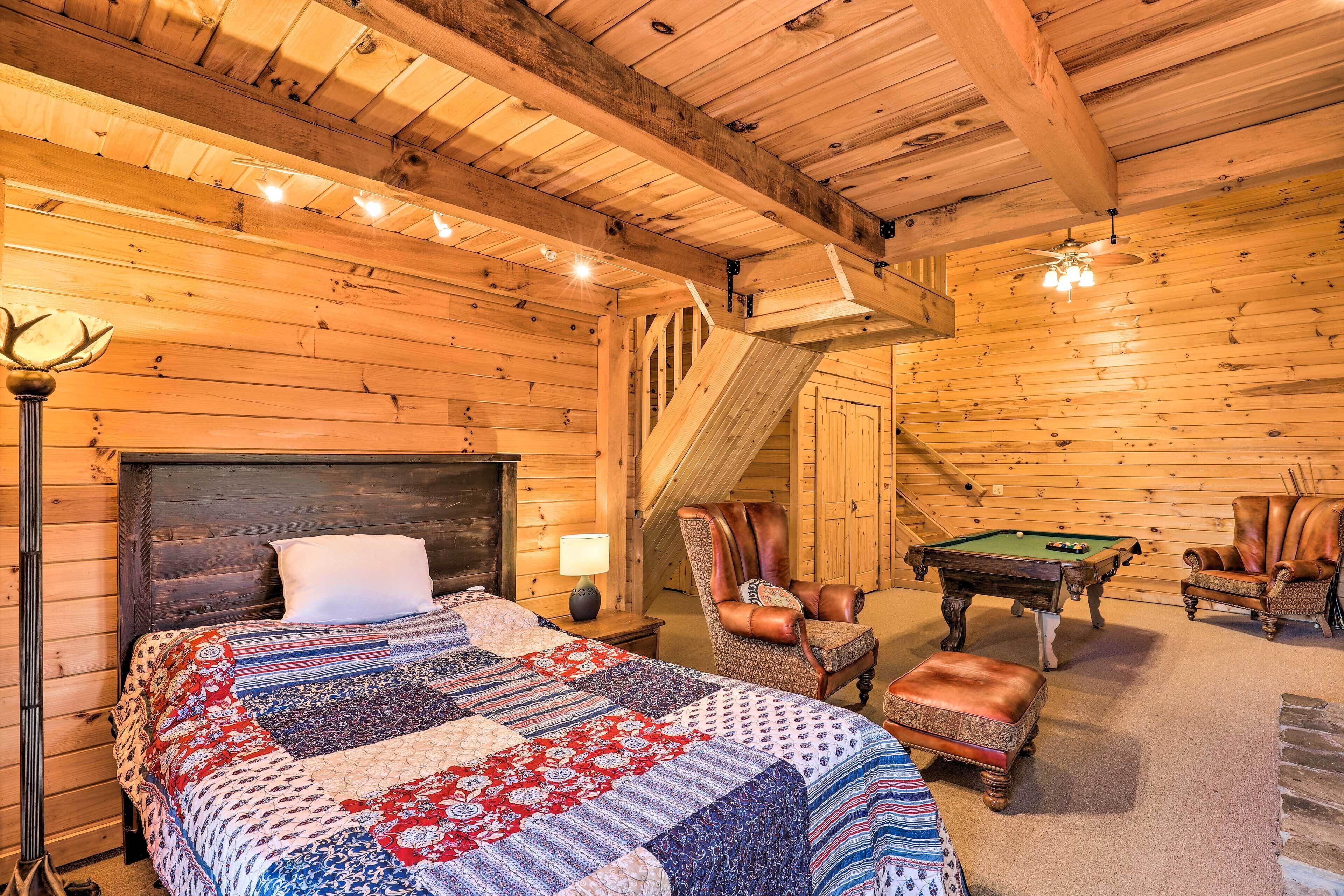 A log cabin interior with a bed, a chair, a pool table, and a staircase.