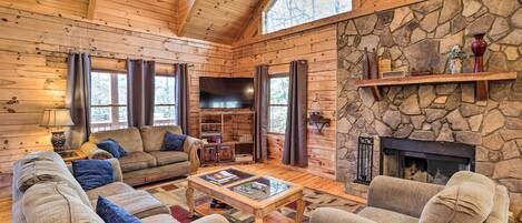 L’intérieur chaleureux d’un chalet en bois, avec une cheminée en pierre, des murs en bois et un grand téléviseur à écran plat.